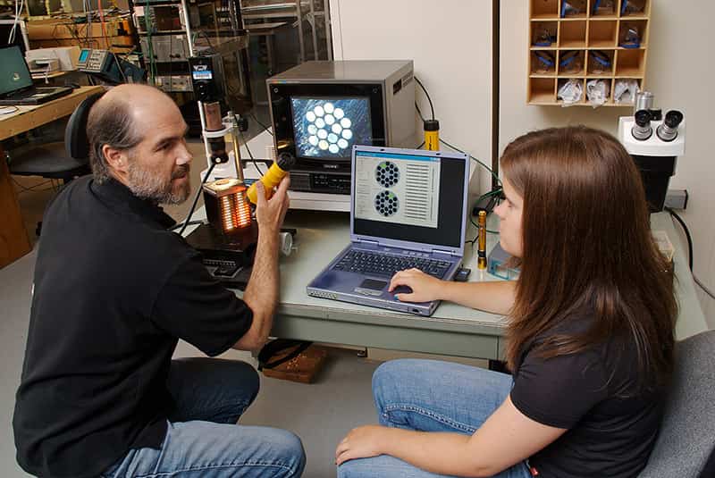 A teacher and a student have a conversation sitting at a computer desk.