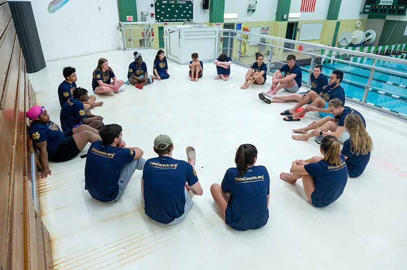 A group of people sit in a circle near an pool.