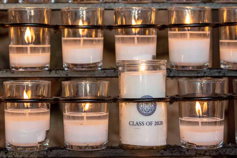 Eight lit candles, one taller than all of the others and has a label that says Class of 2020 and the University of Notre Dame seal.