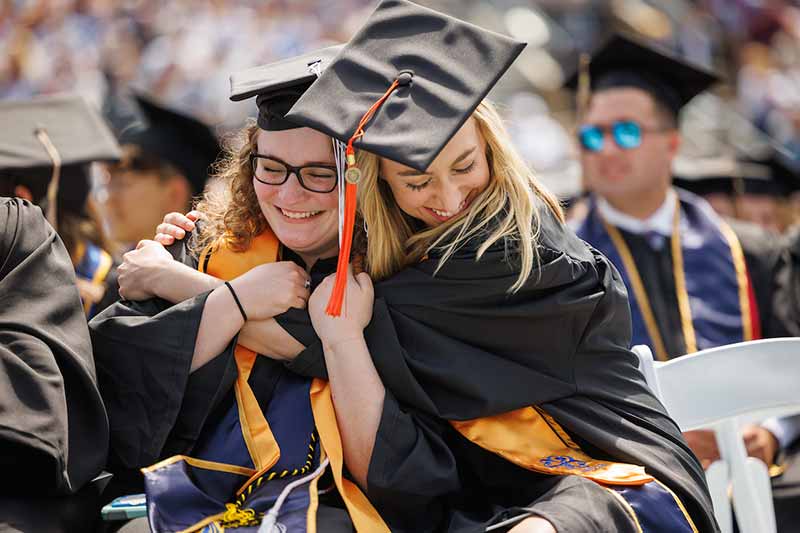 Two women wearing caps and gowns hug.