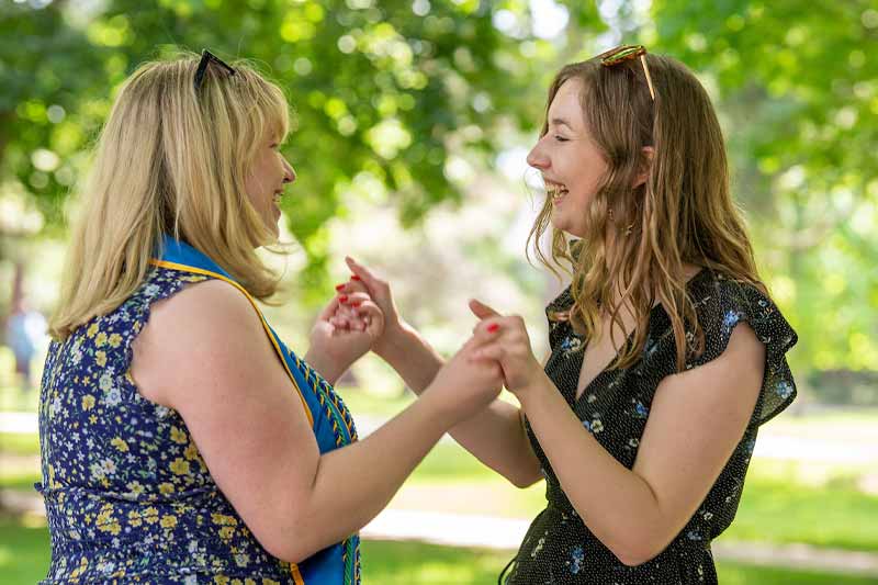 A mother and daughter look at each other laughing and holding eachothers hands.