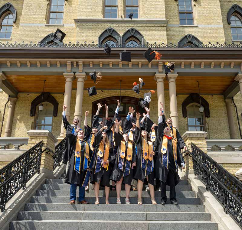 Graduates toss their caps in the air on the steps of the Main Building.