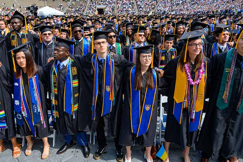 Graduates wearing black graduation robes sing the Alma Mater at the end of the 2022 Commencement ceremony.