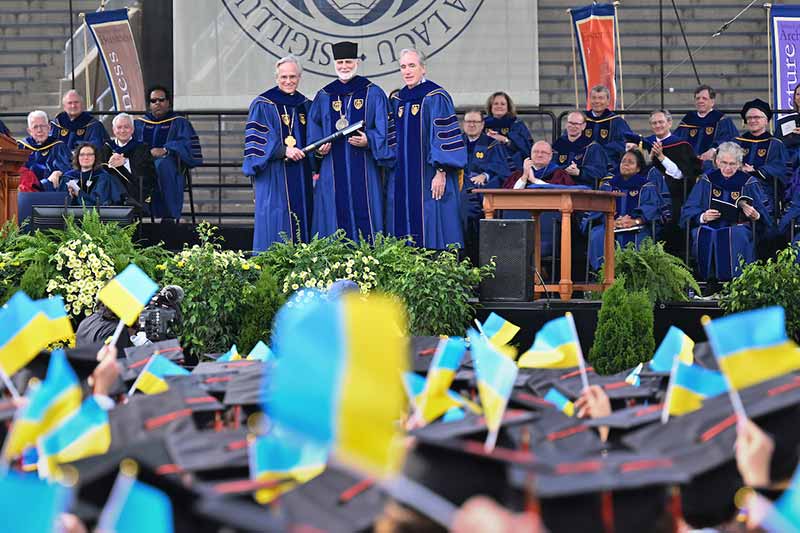 Graduates wave Ukrainian flags in tribute to Archbishop Borys Gudziak as he receives an honorary degree at the 2022 Commencement ceremony.