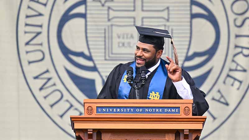 Jerome Bettis, a Black man wearing a black graduation robe speaks at a podium.