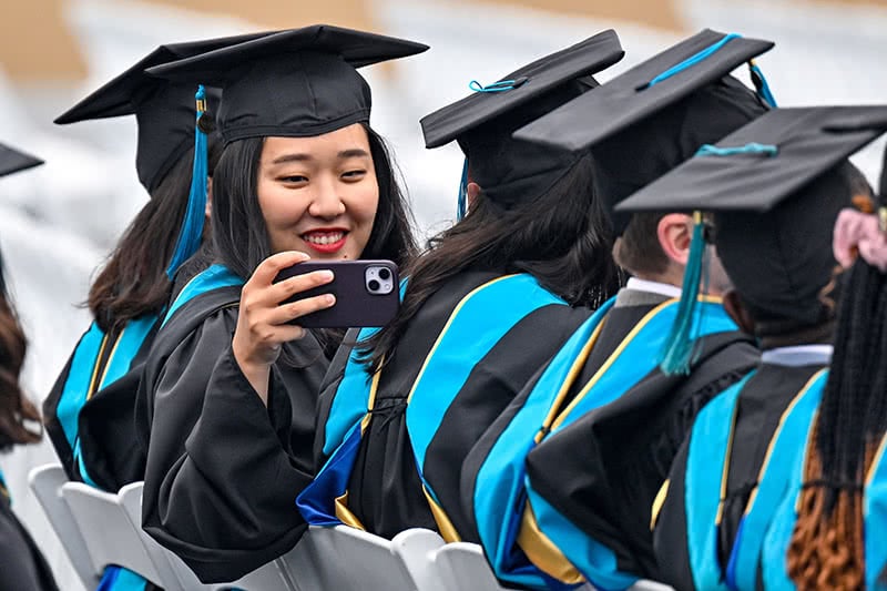 A graduate turning around in her seat to take a photo with her phone.