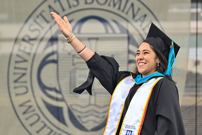 Graduate of Grad School smiles and waves after receiving diploma.