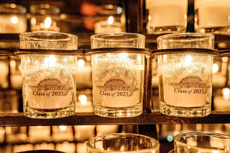 A row of candles at the grotto with printed transparent stickers reading: Class of 2023
