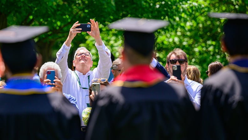 A relative of a graduate holding their phone in the air to capture a photo with graduates out of focus in the foreground.