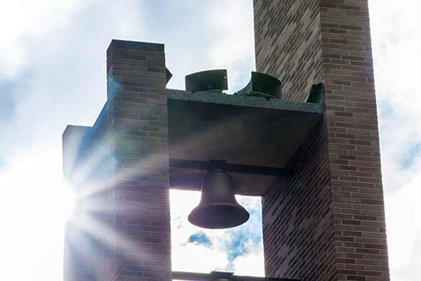A church bell tower with the sun peeking out from behind.