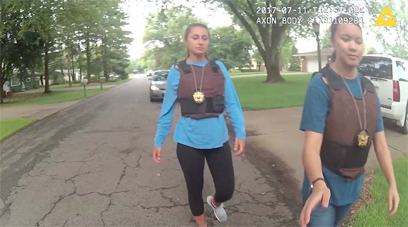 Christina Casino and Mariah Donley pull supplies out of a police car before entering the residence. They wear bulletproof vests and badges.