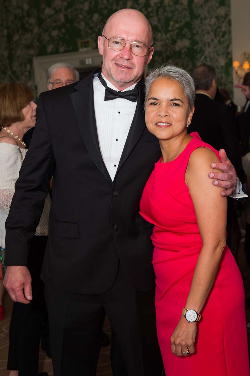 A portrait of Marie Lynn Miranda in a red dress with her husband Chris Geron in a tuxedo.