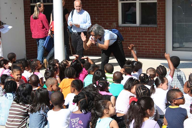 Marie Lynn Miranda gives high fives to a group of children in front of a building.