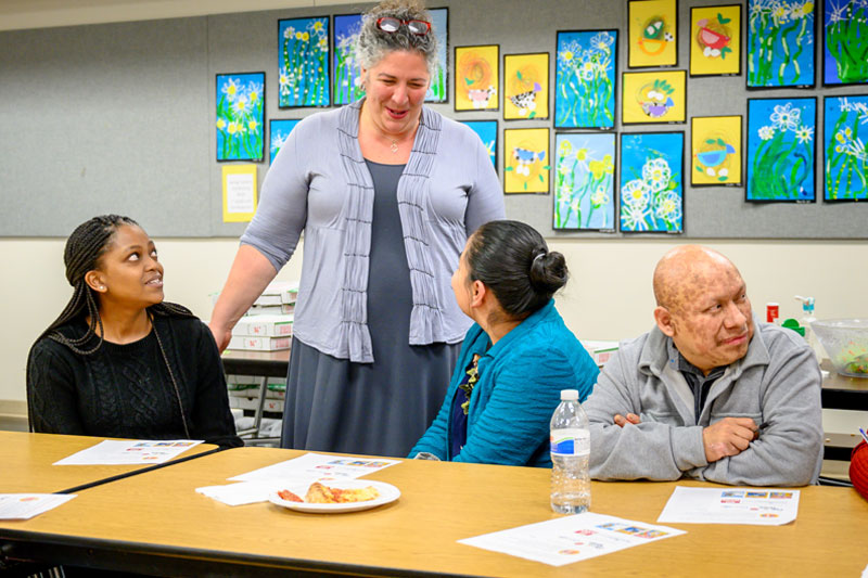 Two Notre Dame students engage in conversation with professor Elena Mangione-Lora as she smiles down at them.