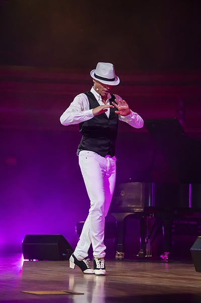 Flamenco dancer Jaime El Estampio, dressed in a white fedora, white pants, and a black satin vest over a white collared button-down, performs onstage at the DeBartolo Performing Arts Center.