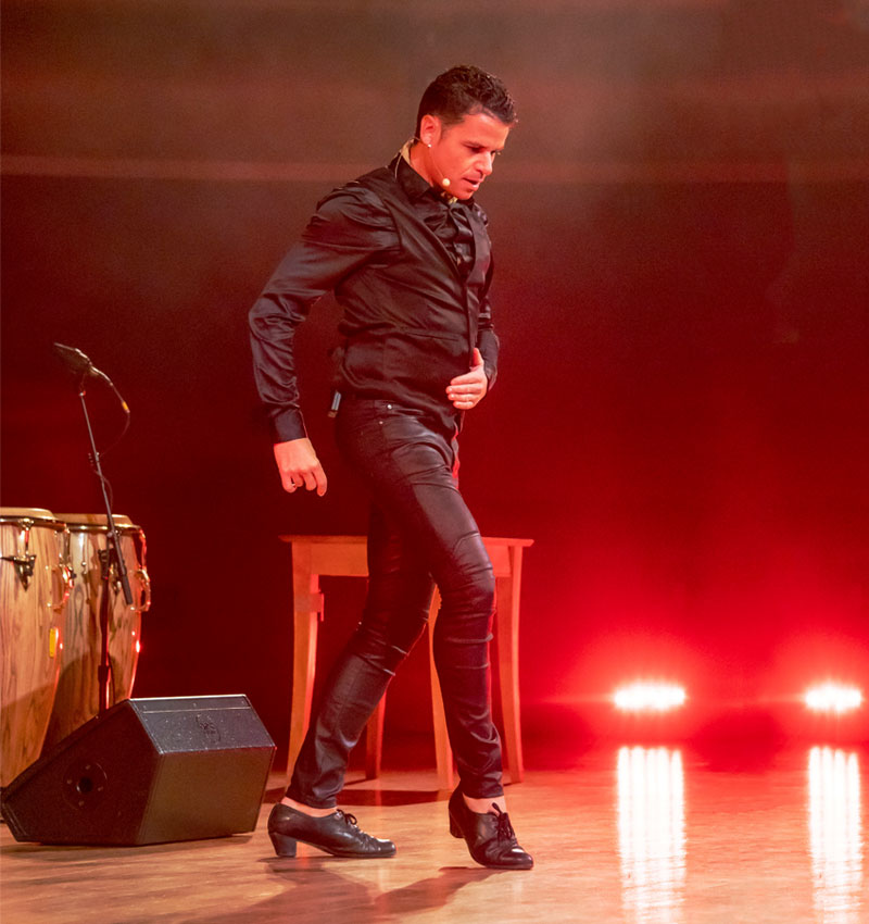 Jaime El Estampio wears all black and stands in a flamenco posture while performing onstage.