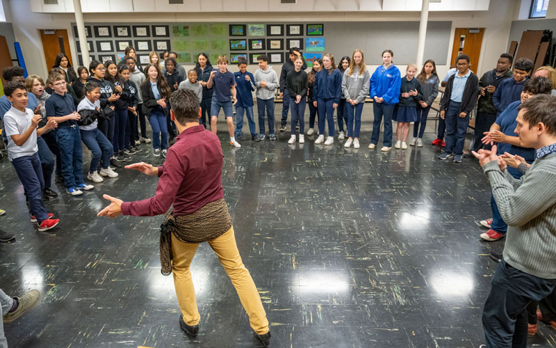 A group of middle school students form a half circle around Jaime El Estampio while he shows them flamenco moves.