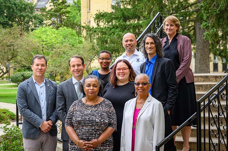 A group of faculty pose for a photo outside on cement stairs.