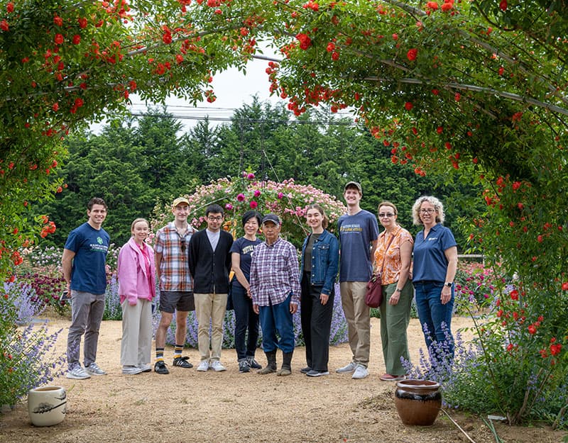 Notre Dame faculty and students pose with Yoshitomo Yokota under a rose-filled trellis.
