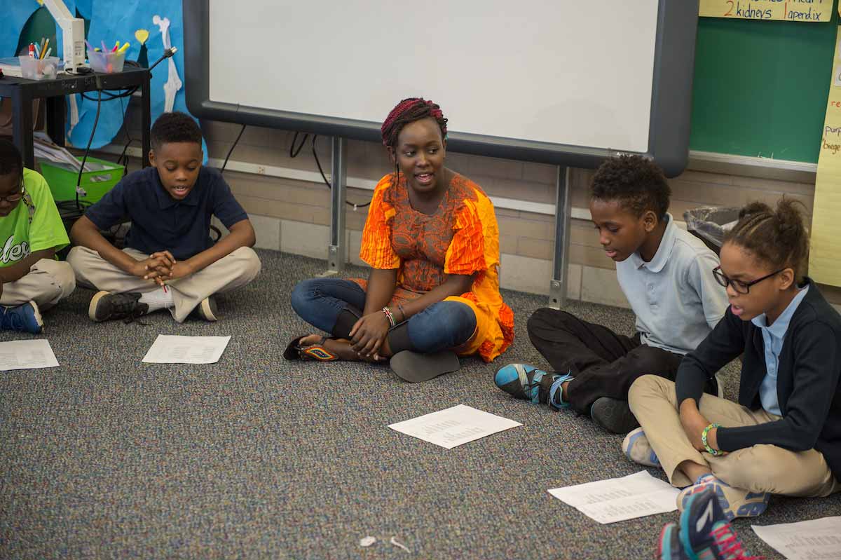 Kenyan FLTA Laureen Owaga sits with a fourth-grade class as they sing a song in Swahili.