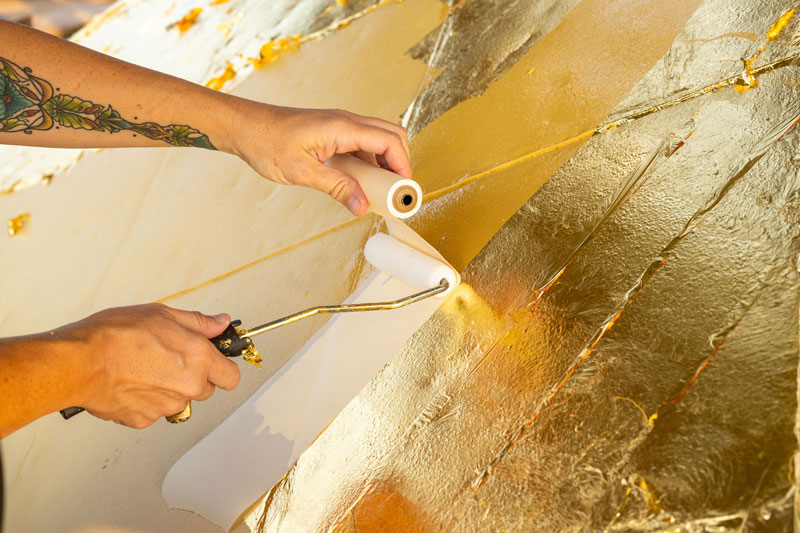 A close up view of a roll of gold leaf being applied to the Golden Dome by a roller. Only the hands of the person applying the gold are in view.