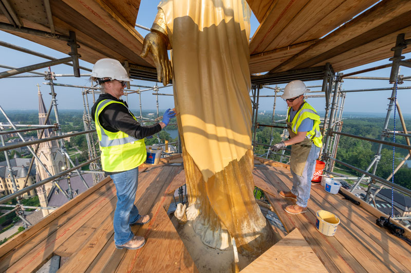 A close up of the statue of Mary on top of the Golden Dome. She has a layer of yellow primer paint on her.