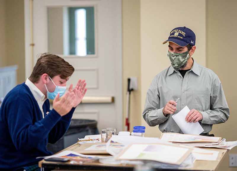 A student working gestures with the professor standing by.