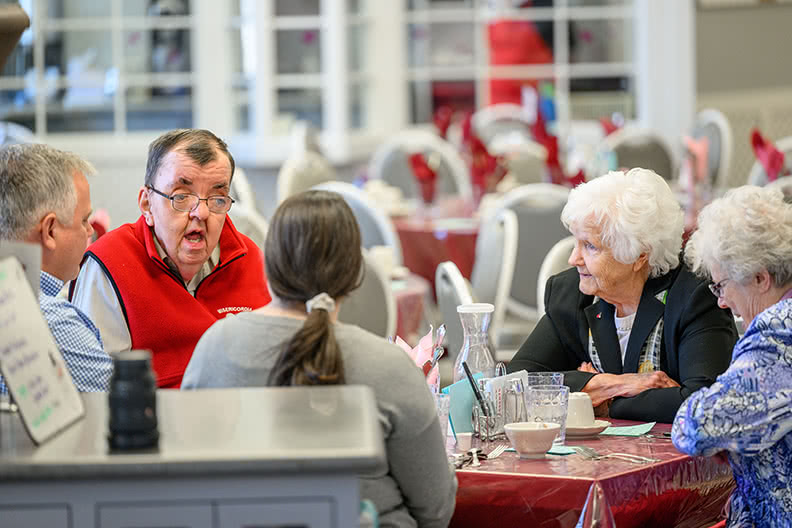 5 people seated at a table eating lunch and in conversation.