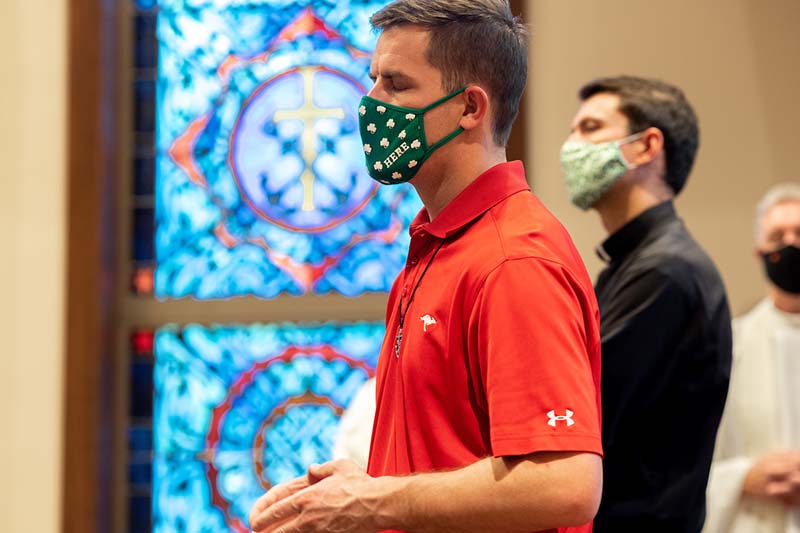 A masked man prays with his eyes closed in the chapel.