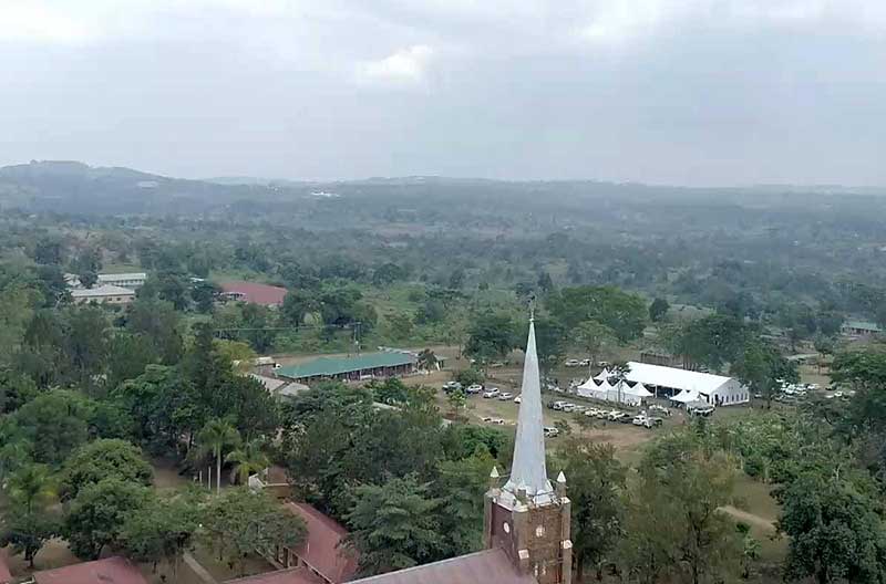 An aerial view of an area of Uganda. A large white tent and several cars parked, surrounded by trees.