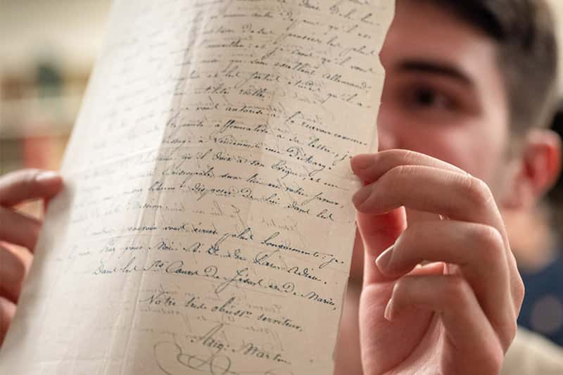 A student holds up a piece of paper up to the light. You can see the calligraphic writing on both sides of the paper.