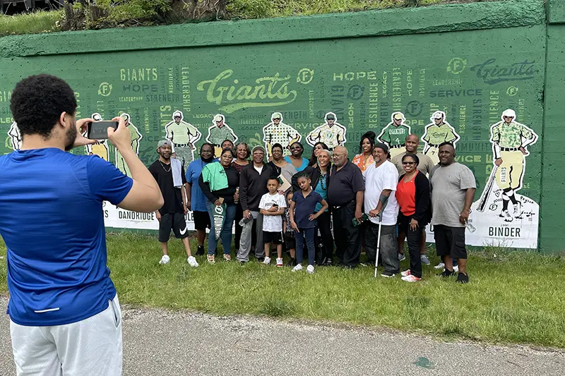 The present-day Poindexter family standing in front of the team mural wall while getting their photo taken.