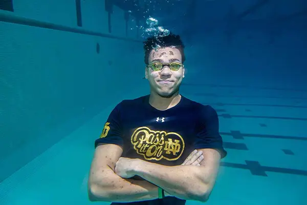 A college student wearing goggles crosses his arms and floats under water
