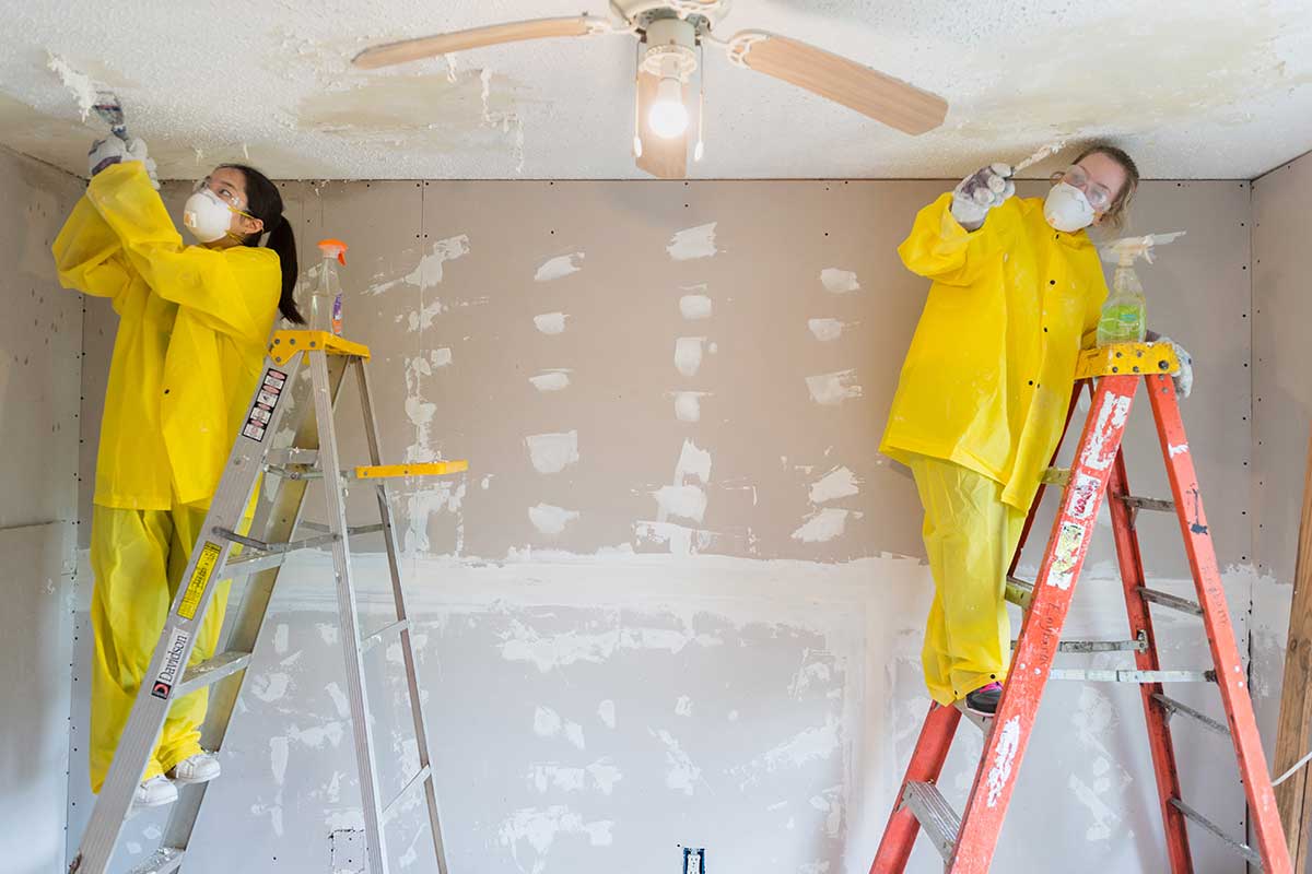 Two students on top of ladders patching walls.