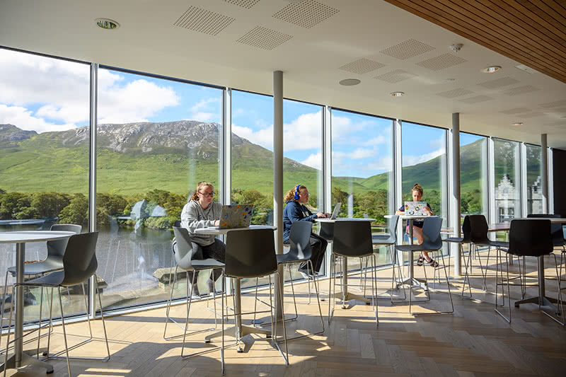 Students working at tables inside a study area in Kylemore with a view of the mountains behind them