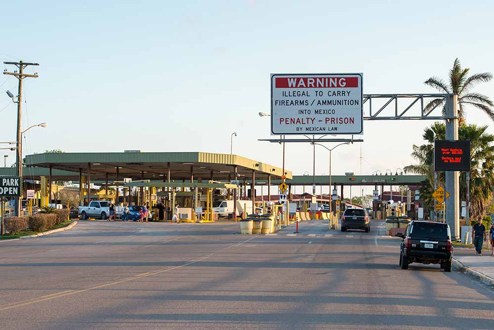 The U.S.-Mexican border with a road sign that says “ WARNING: Illegal to carry firearms/ammunition into Mexico. Penalty - prison by Mexican Law.”