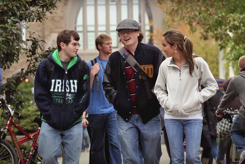 Three students wearing backpacks walk and talk through campus.