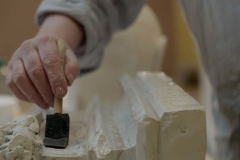 A hand restoring a sculptural plaster cast
