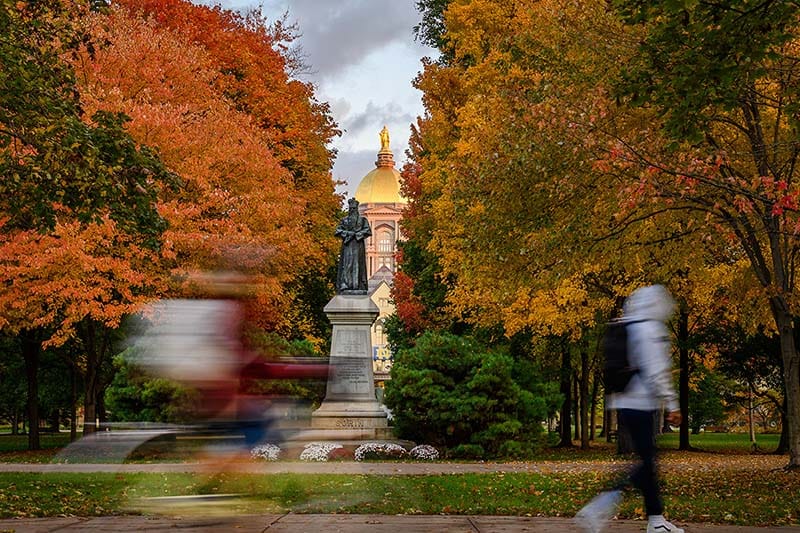 Students walk past the Sorin statue on Main Quad during fall.