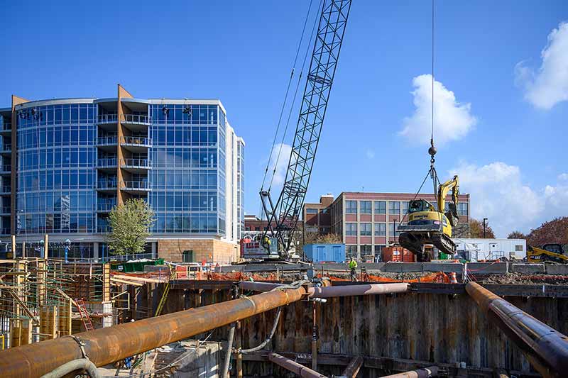 A construction crew works in an area near a downtown. Tall glass buildings in the background.