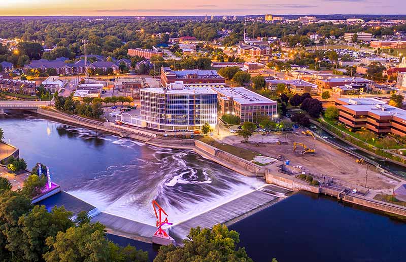 A nighttime photo of downtown South Bend along the St. Joseph River dam. Lights in the city are glowing yellow.