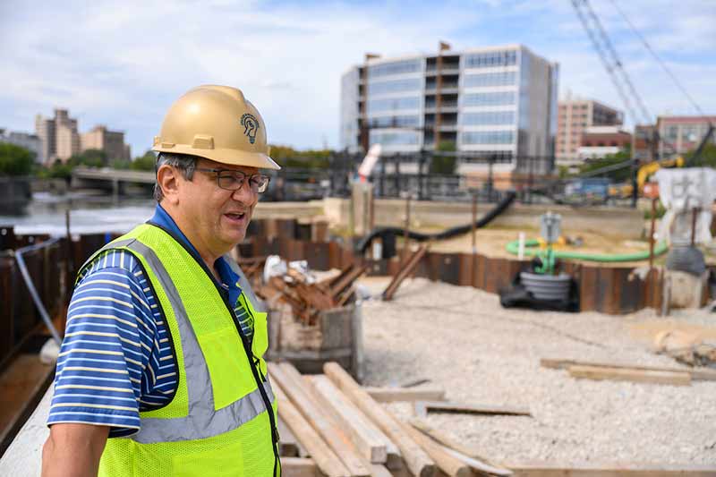 A man wearing a gold hard hat looks off into the distance on a construction site.