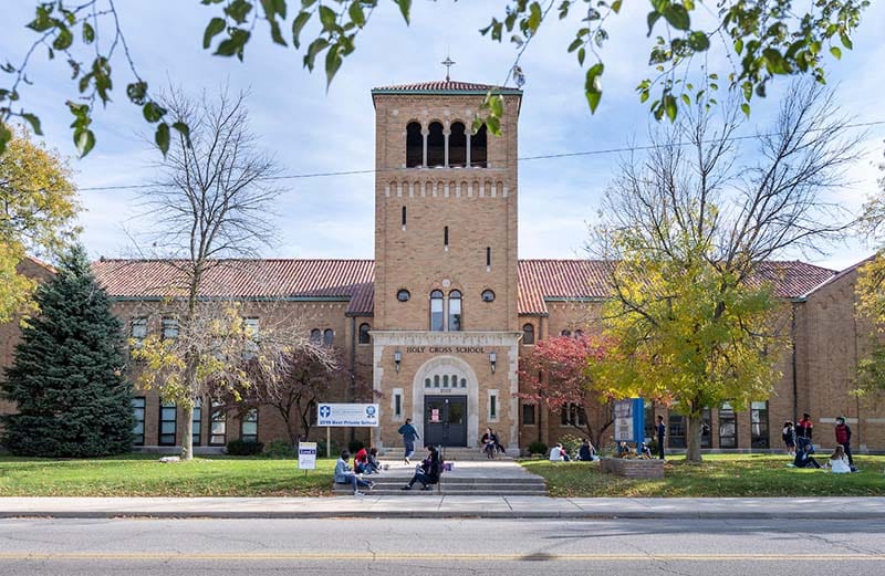 Exterior of Holy Cross School with people on the front steps.