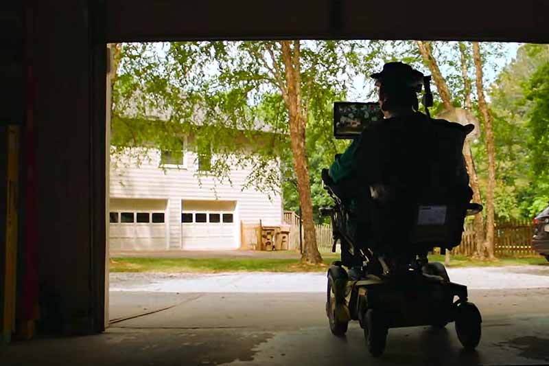 A silhouette of a person in a powered wheelchair leaving a garage.