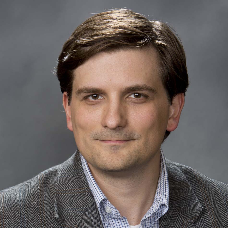 A headshot of a man against a gray background wearing a suit.