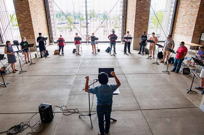 A conductor leads a group of masked singers practicing inside Leahy Gate of Notre Dame Stadium.