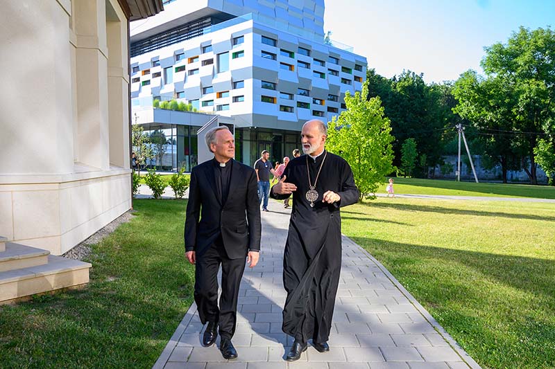 Rev. John I. Jenkins, C.S.C. and Right Reverend Borys Gudziak, both wearing black priestly attire, walk side by side on a sunny day.