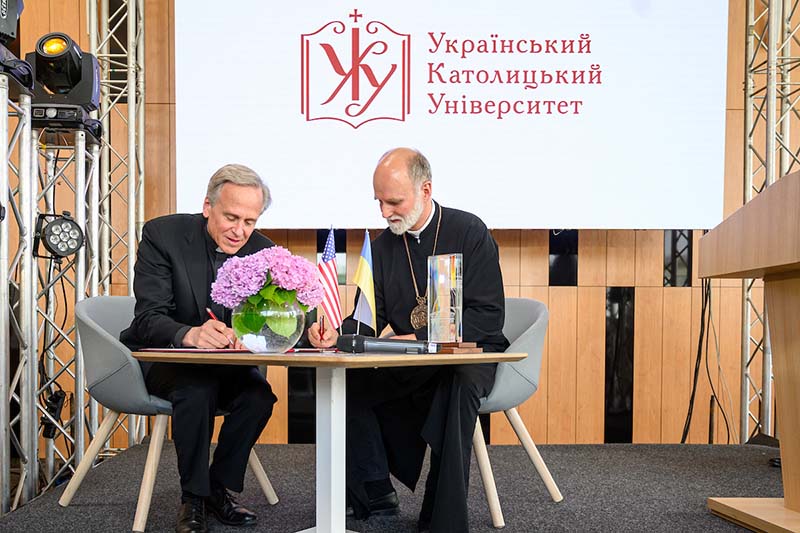 Rev. John I. Jenkins and The Right Reverend Borys Gudziak sit together at a table and sign a document. The Notre Dame Award is on the table.