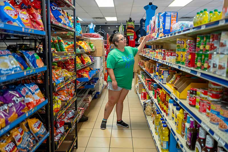 A woman looks at the top shelf of groceries in a small convience store.