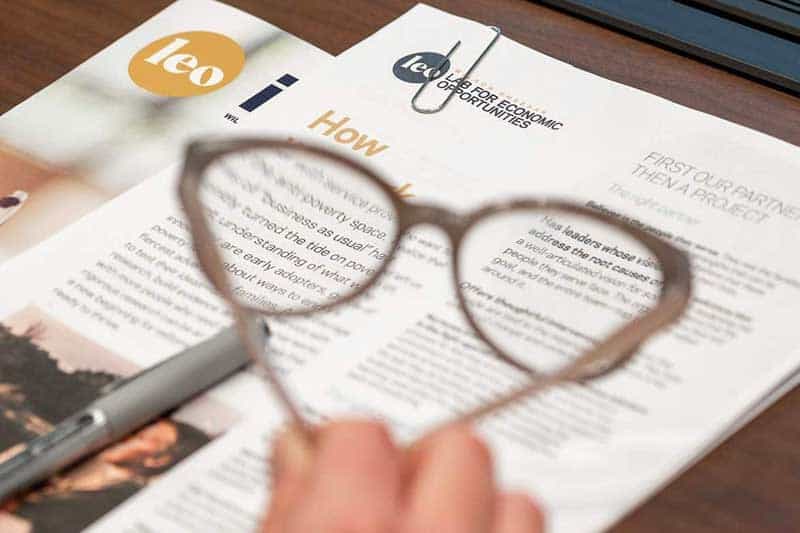 Papers and booklets on a desk and glasses in blurred in the foreground.